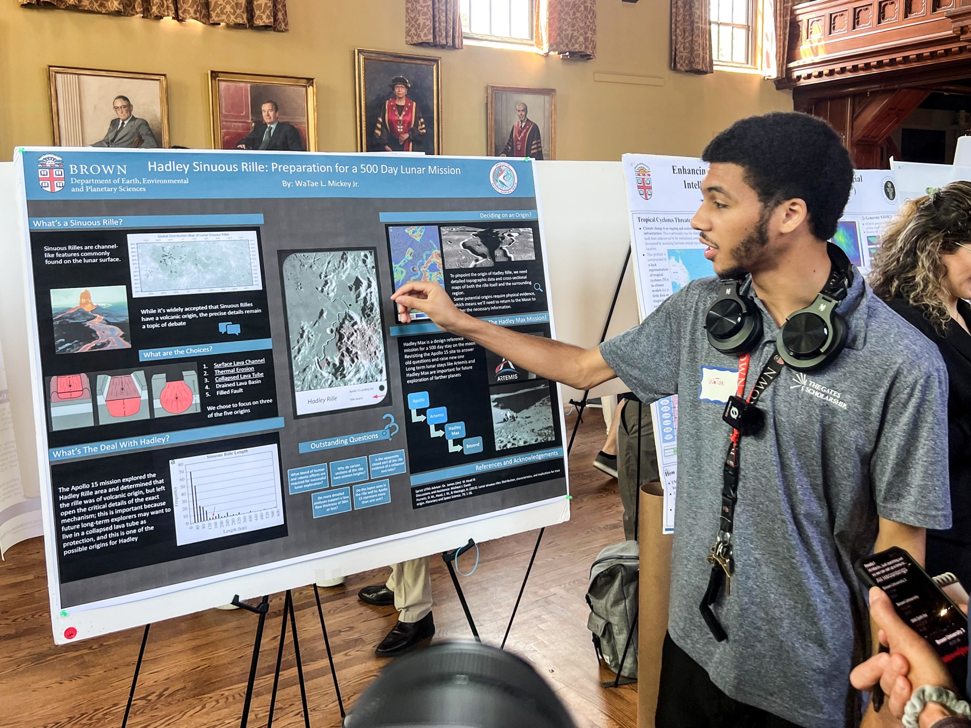 Male research student points to a photo of the lunar surface as he describes channel-like features commonly found on the moon.